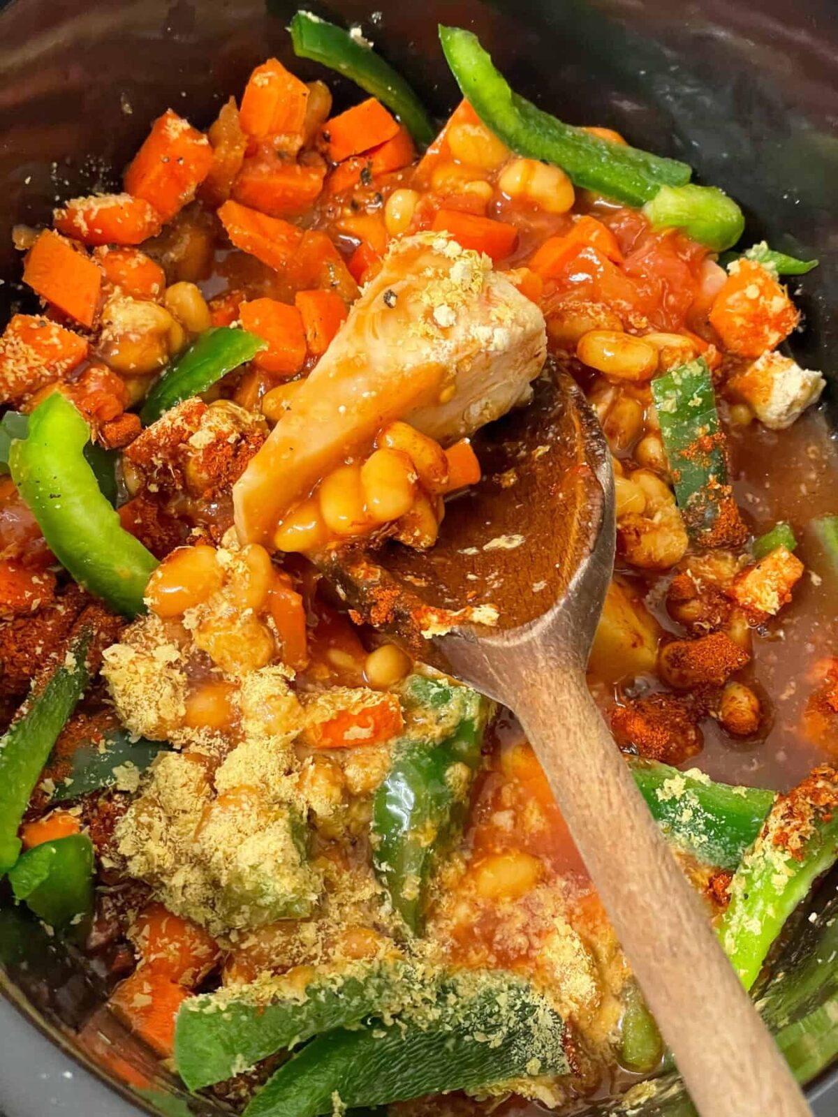 camp fire stew ingredients in slow cooker with wooden spoon to side.