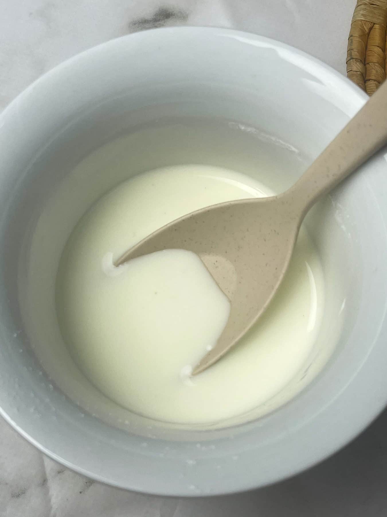 Cornflour slurry prepared in white bowl with cream coloured spoon.