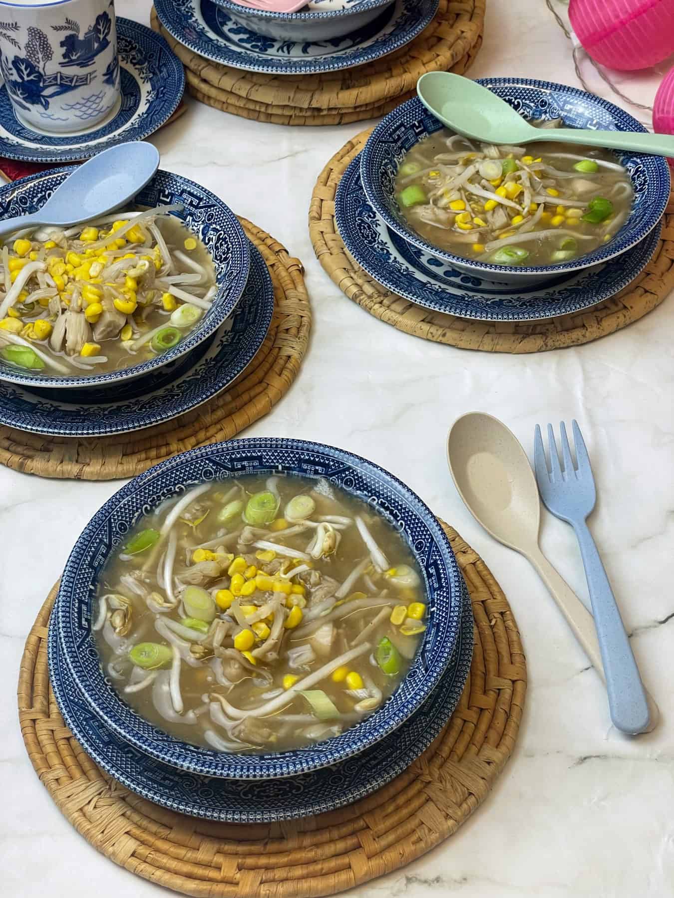 Three bowls of vegan Chinese soup served in blue Chinese patterned bowls with matching cup in background, white marble tablecloth background.