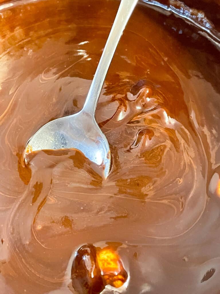 Chocolate, syrup and margarine melted in saucepan with metal spoon stirring the mix.