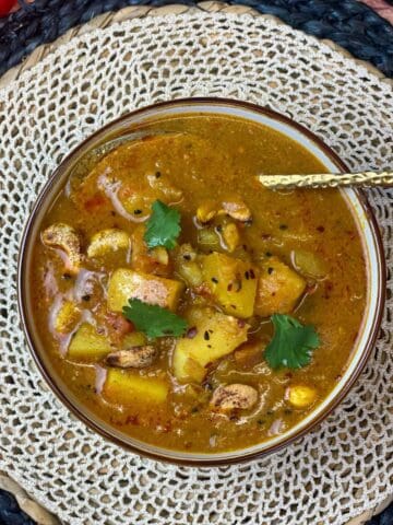 A bowl of Bombay curry soup sitting on a straw matt with a gold spoon in the bowl.