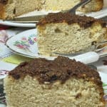 two slices of cinnamon streusel topped cake on small flower patterned plates, whole cake in background with cake slice.