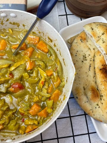 A bowl of curry with vegetables and bread on a table