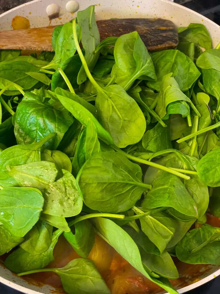 fresh spinach added to the pan with potatoes cooking.