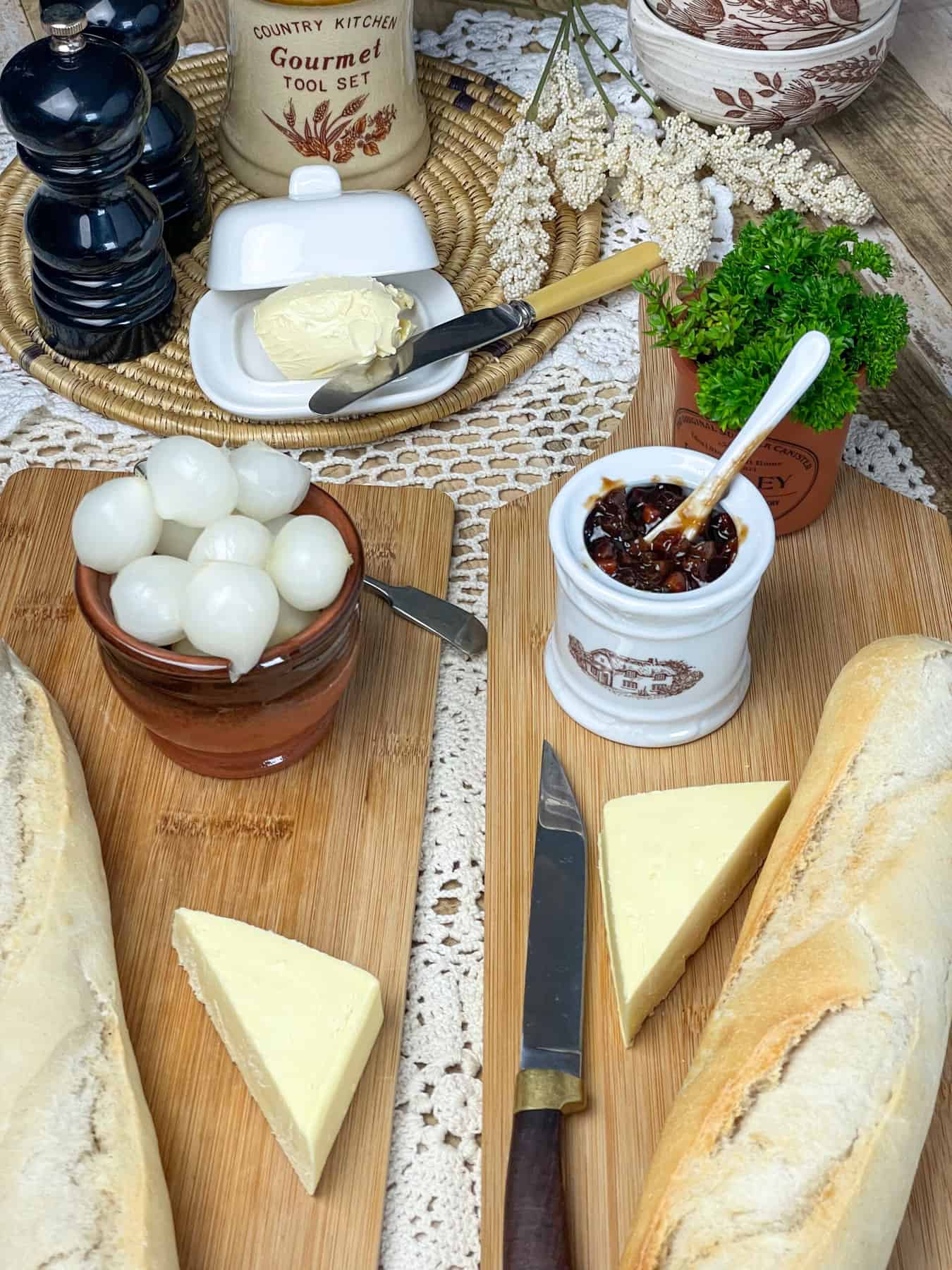 Cutting boards with baguettes, bowls of pickled onions, small dish with chutney, and black salt and pepper shakers to side.