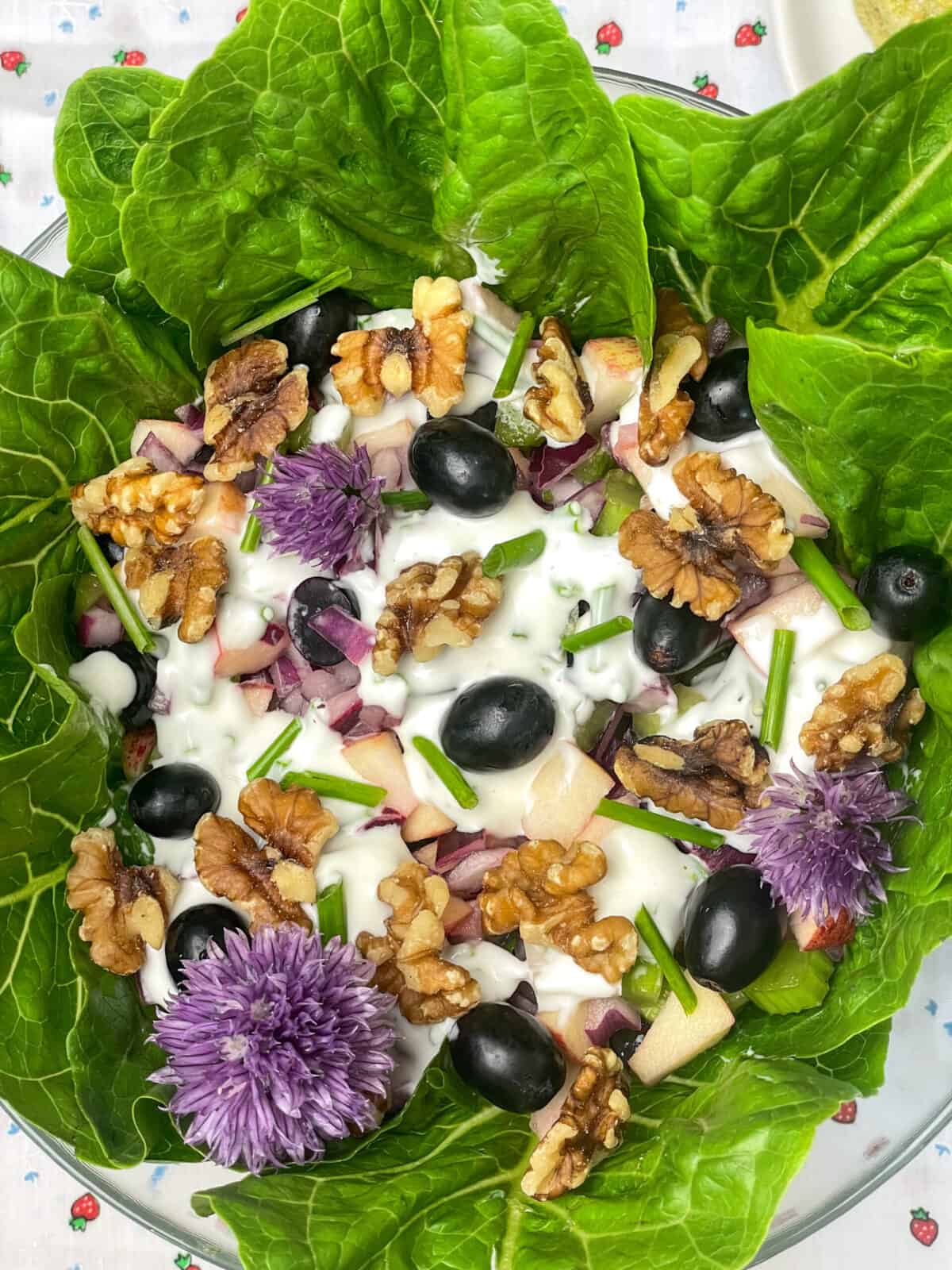 Close up photo of vegan Waldorf salad in bowl, with white and strawberry patterned tablecloth background.