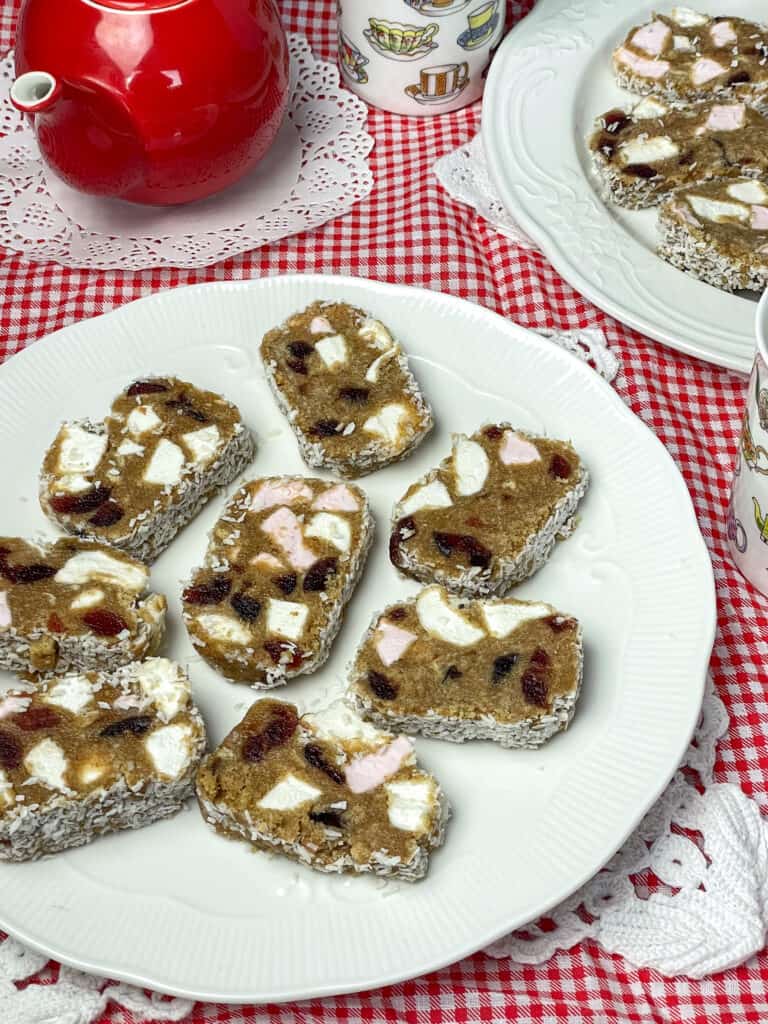 White cake plate with fifteens, second plate of fifteens to side, red teapot to side and cup with cup images beside teapot, red and white check background.