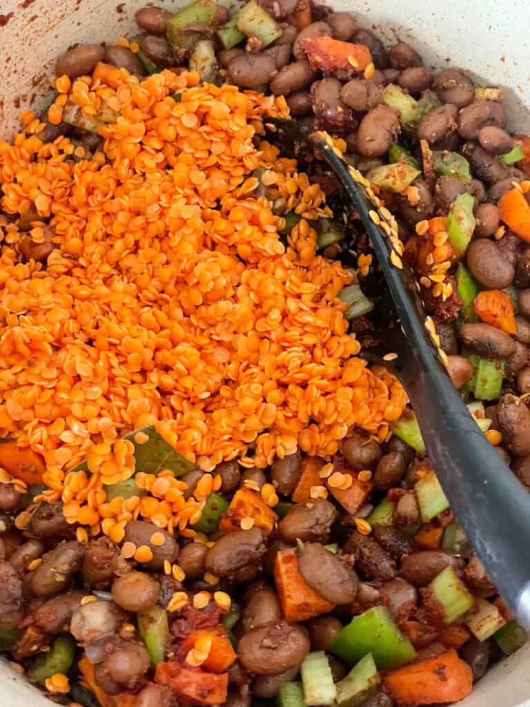 red lentils added to red beans stew in saucepan with black ladle.