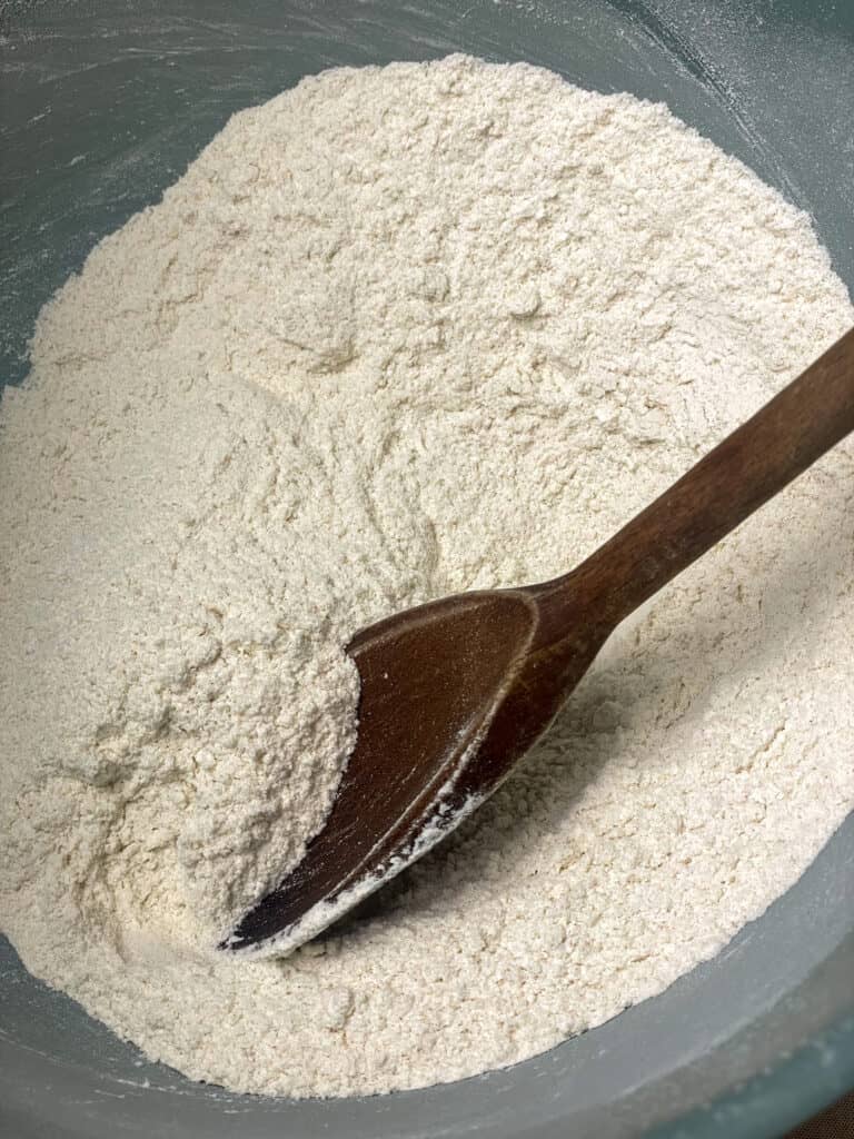 flour added to turquoise coloured mixing bowl with wooden spoon.