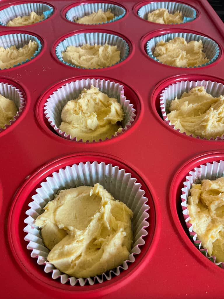 cake batter shared out between 12 cup muffin baking tray lined with paper cases.