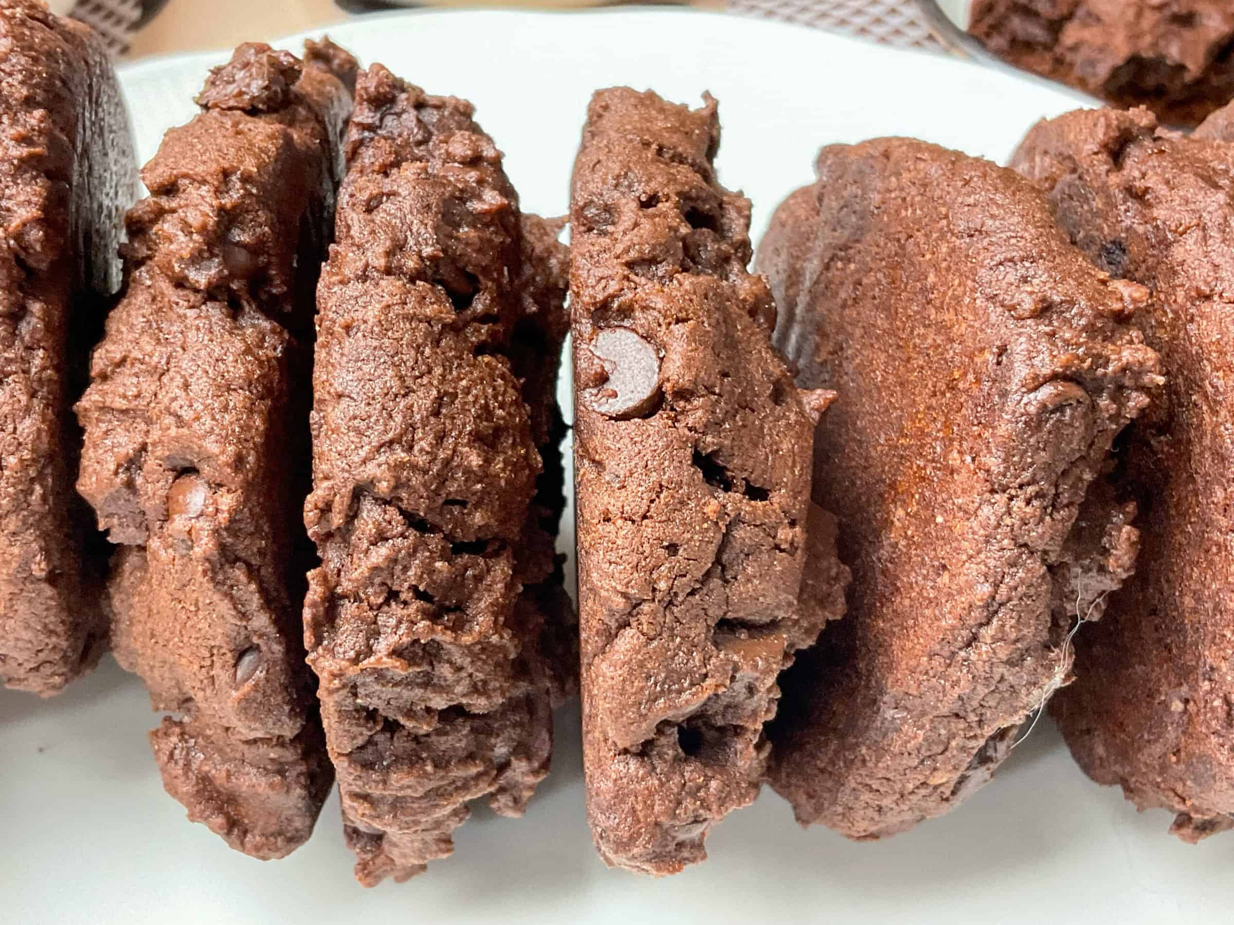 A pile of double chocolate chip cookies on their side with the edges showing, on a white plate.