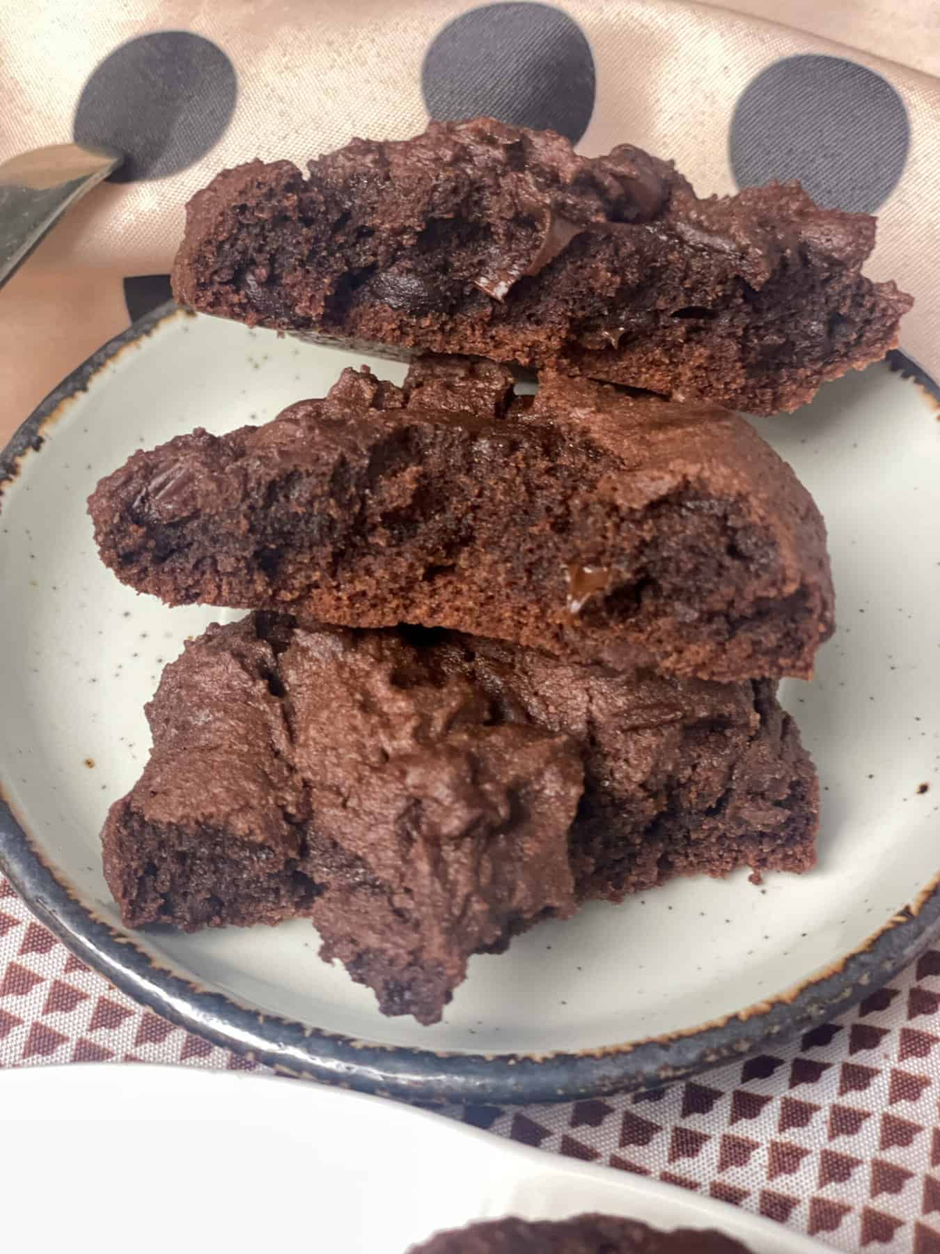 A small plate of cookies that have been split in half so the gooey insides are revealed, brown spotty table cloth background.