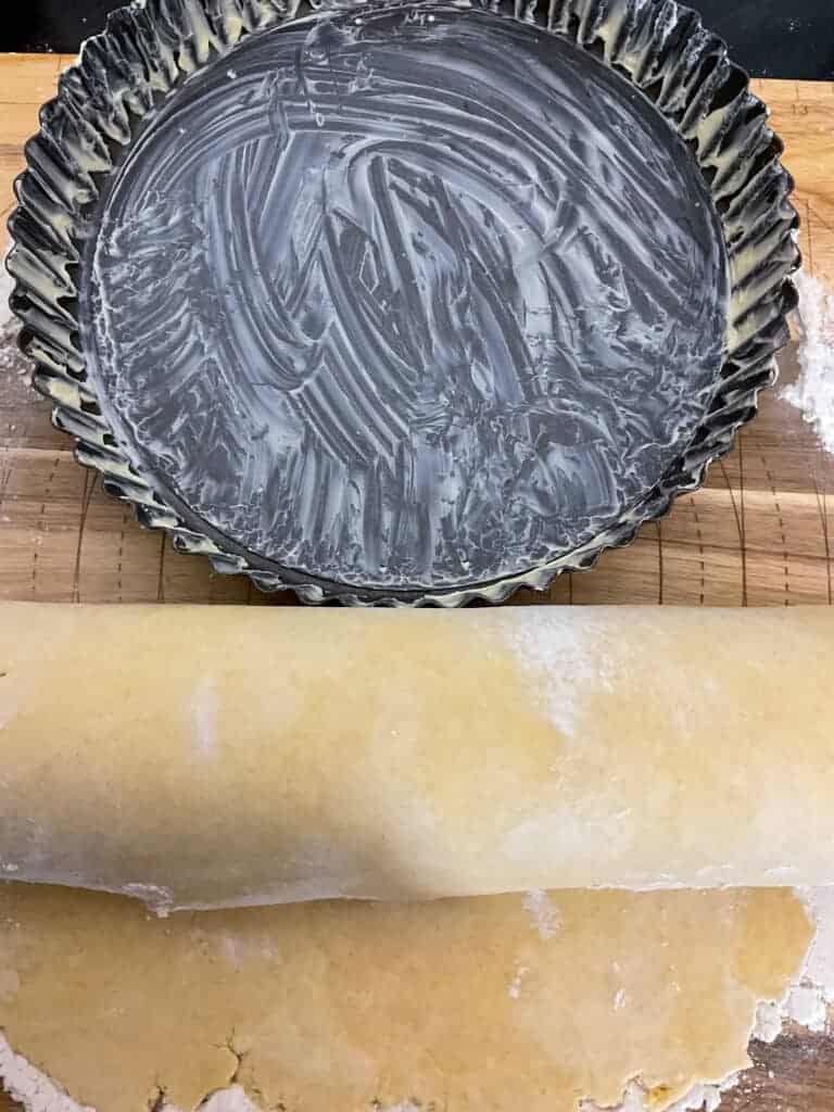 Pastry dough wrapped around rolling pin beside greased flan dish.