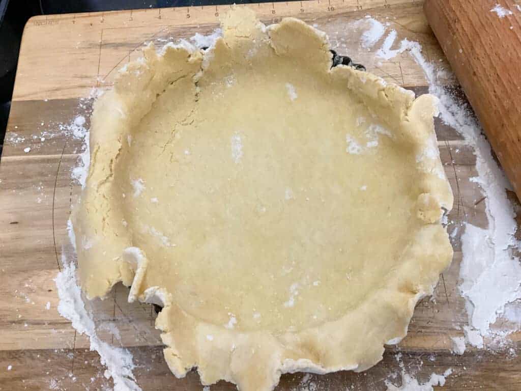 Pastry dough in flan dish on wooden board.