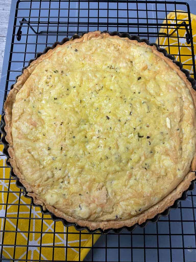 Baked vegan cheese flan on wire rack with yellow oven mitt underneath.