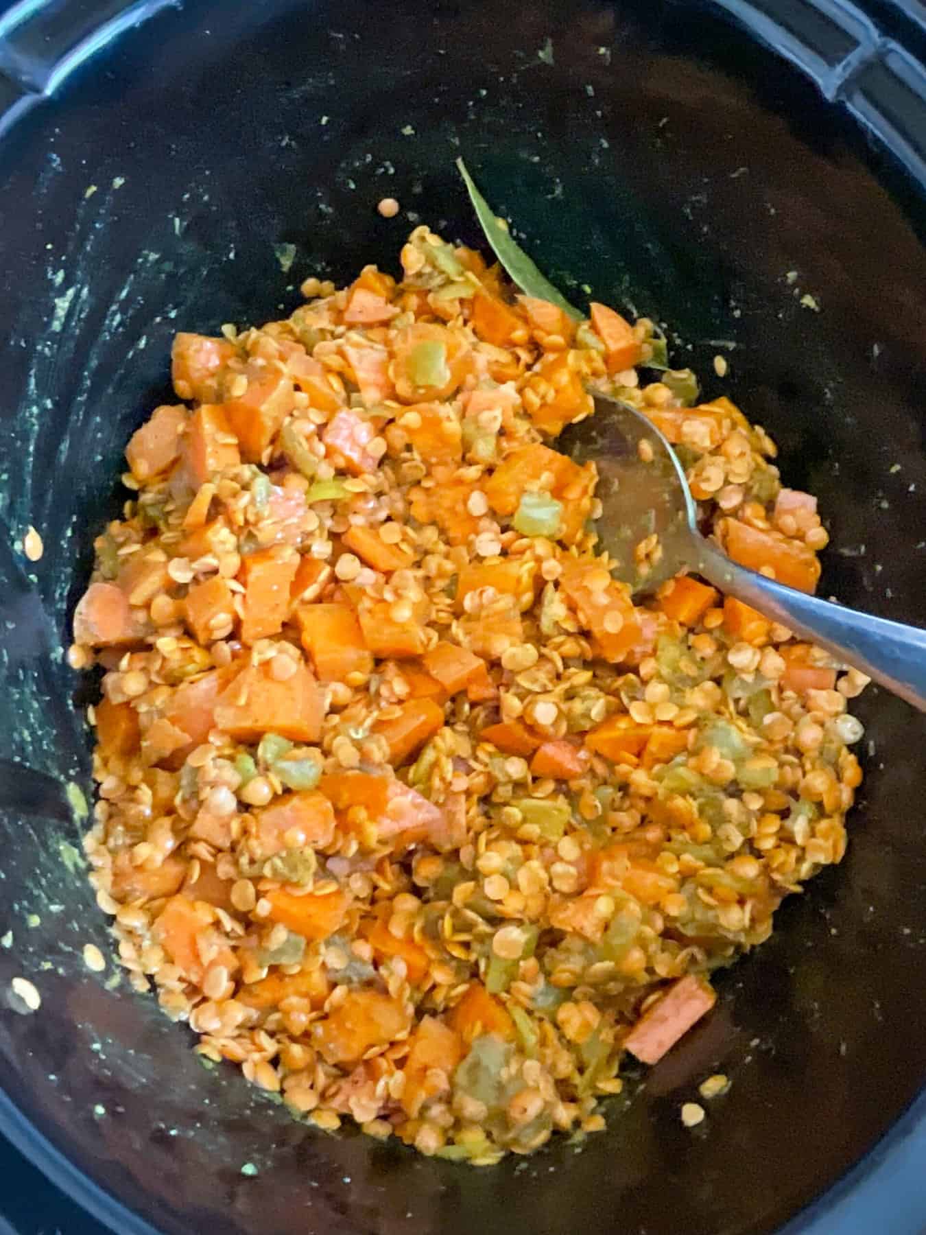 Red lentils mixture mixed up in slow cooker with silver spoon.