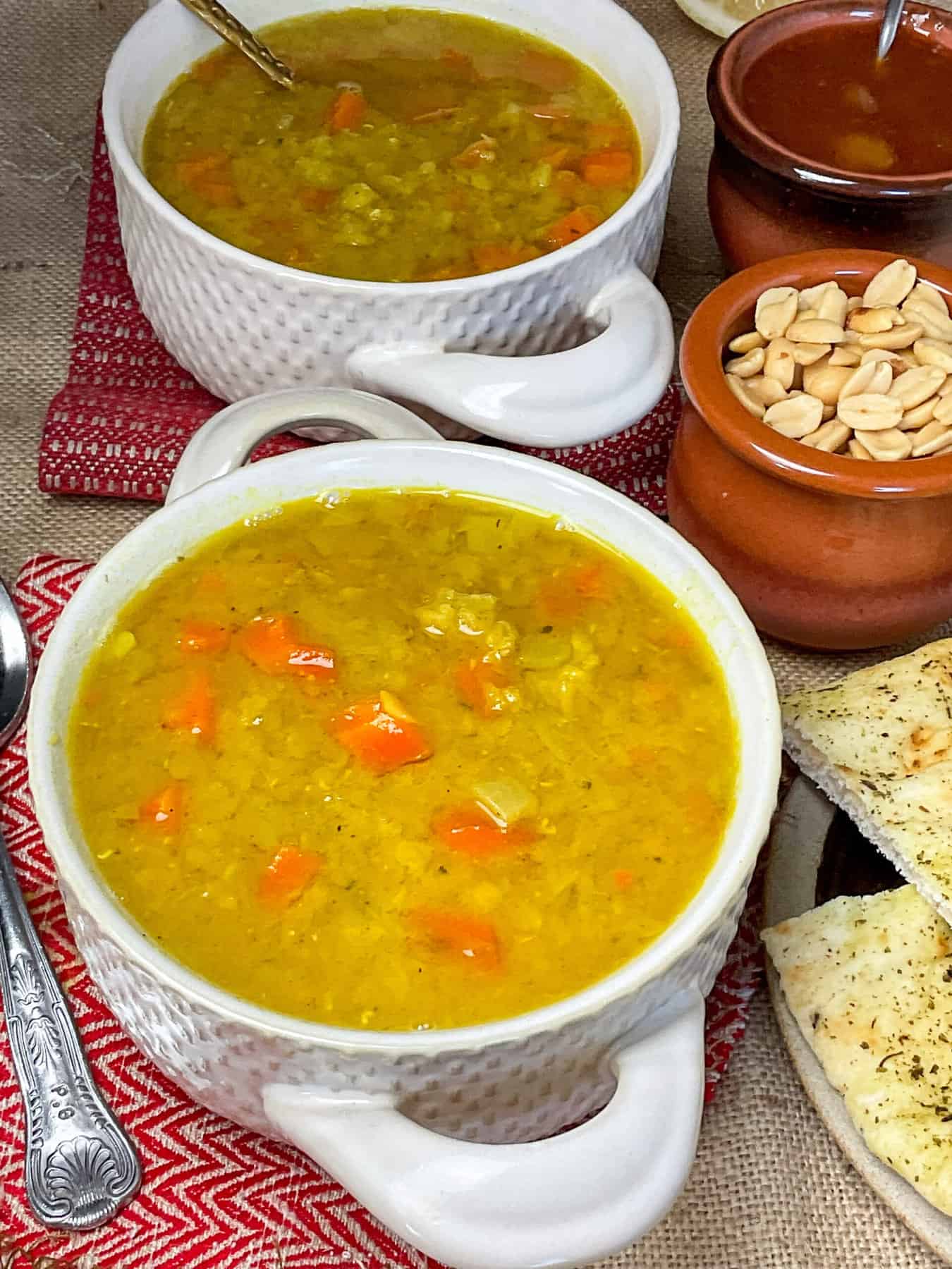 Soup served in bowls with small bowls of various garnishes to side, red tea cloth background.