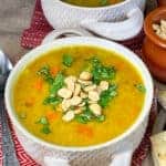 Two bowls of slow cooker red lentil dal soup in double handled bowls, with red soup matts, silver spoon to side, and brown burlap background.