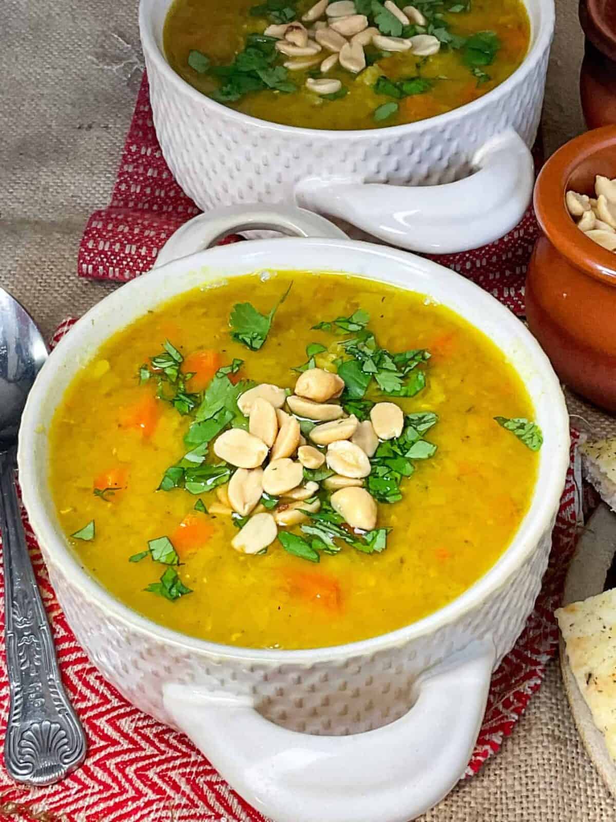 Two bowls of slow cooker red lentil dal soup in double handled bowls, with red soup matts, silver spoon to side, and brown burlap background.