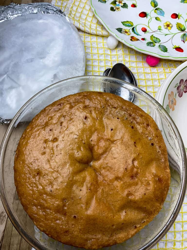 cooked steamed jam pudding with lid removed and flower serving plate in background, yellow tea towel.