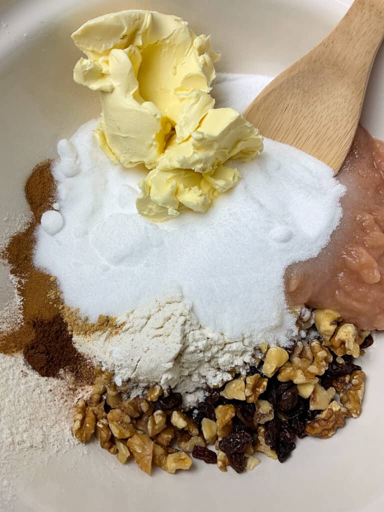 applesauce spice cake ingredients added to mixing bowl with wooden spoon.