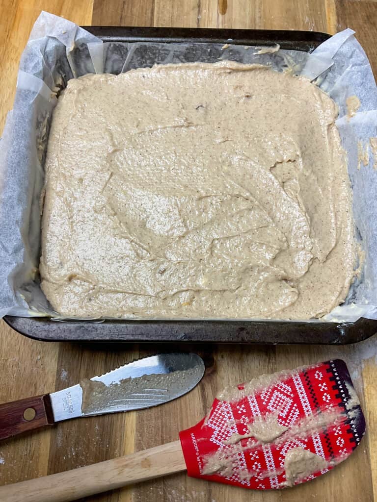 applesauce cake batter in baking tin on a wooden board with two spatulas to side.