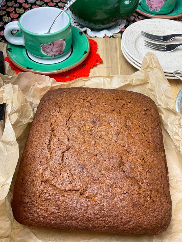 applesauce cake baked and on top of crinkled baking paper, with tea cup and saucer to side, and cake plates.