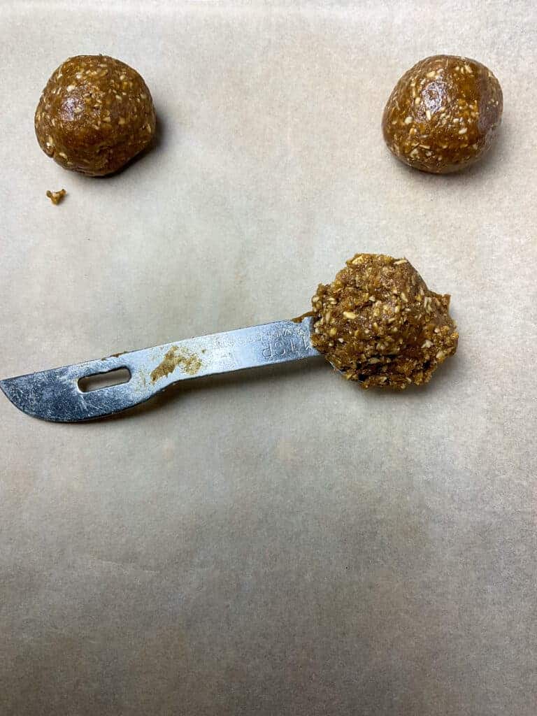 Biscuit dough scooped up in a teaspoon measurer and sitting on baking sheet with two biscuit dough balls.