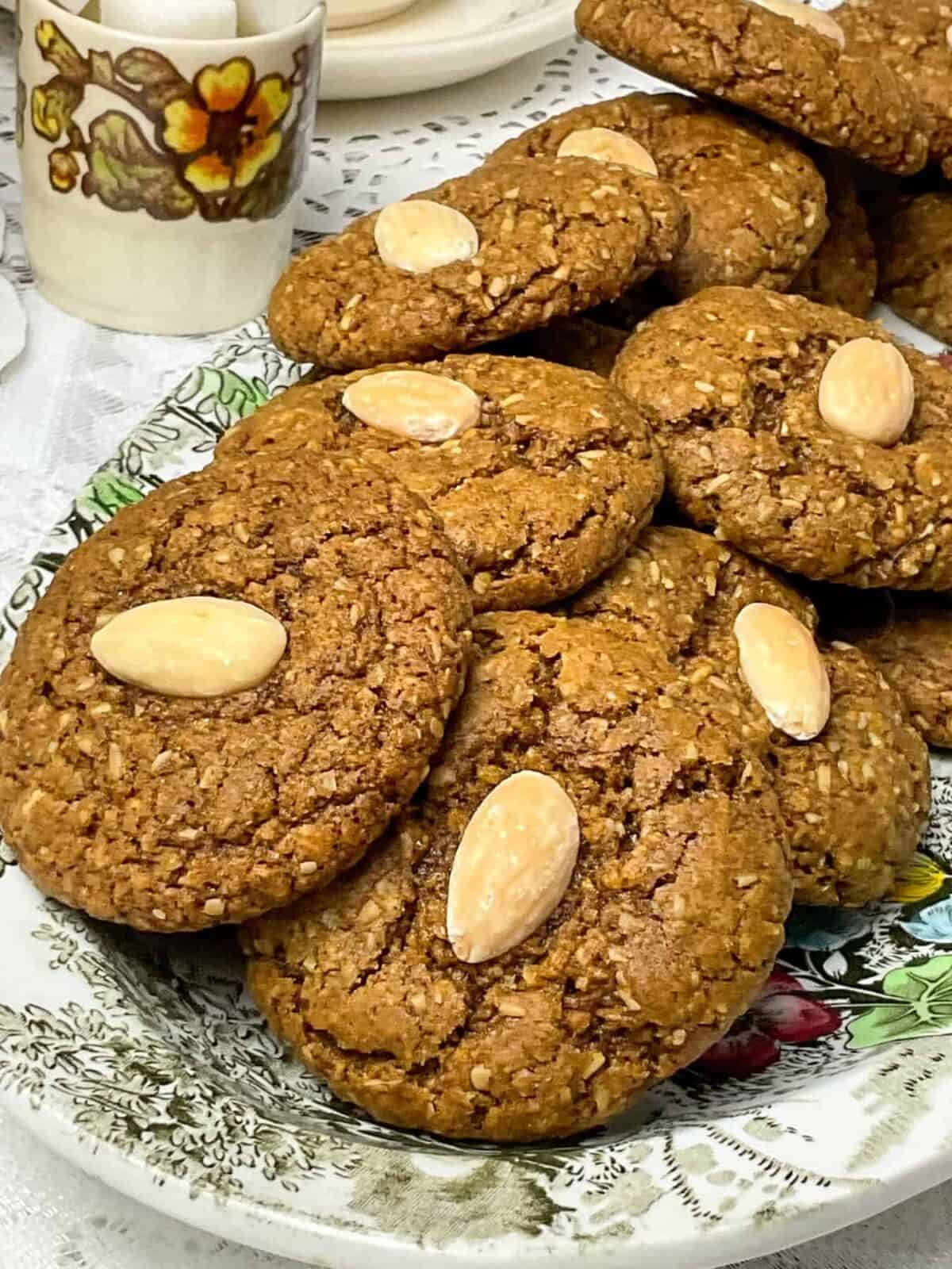 Traditional parkin biscuits on a flower patterned plate, with small sugar cube dish to side and white doily tablecloth.