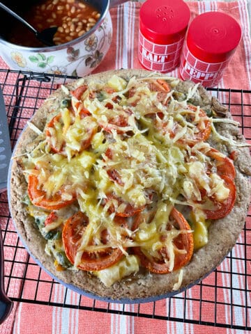 Close up of vegan British homity pie on a wire rack, with red and white striped tea towel underneath, red and white salt and pepper shakers to side with a flower imaged saucepan with baked beans.