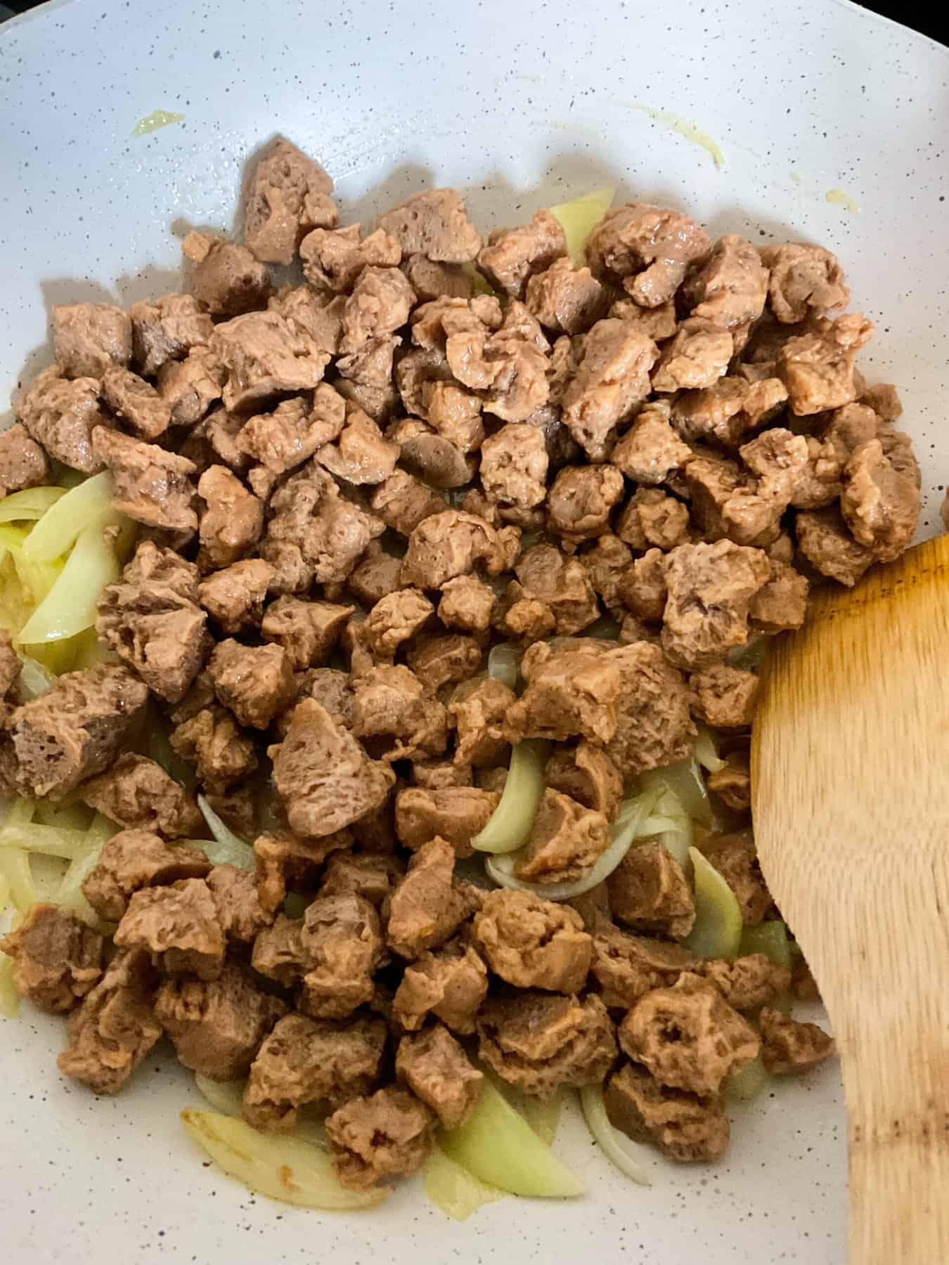 Textured protein chunks in cream coloured cooking pan with wooden spatula to side.