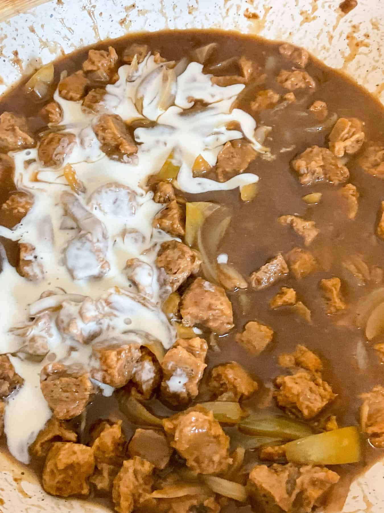 Sour cream added to cooked vegan stroganoff.