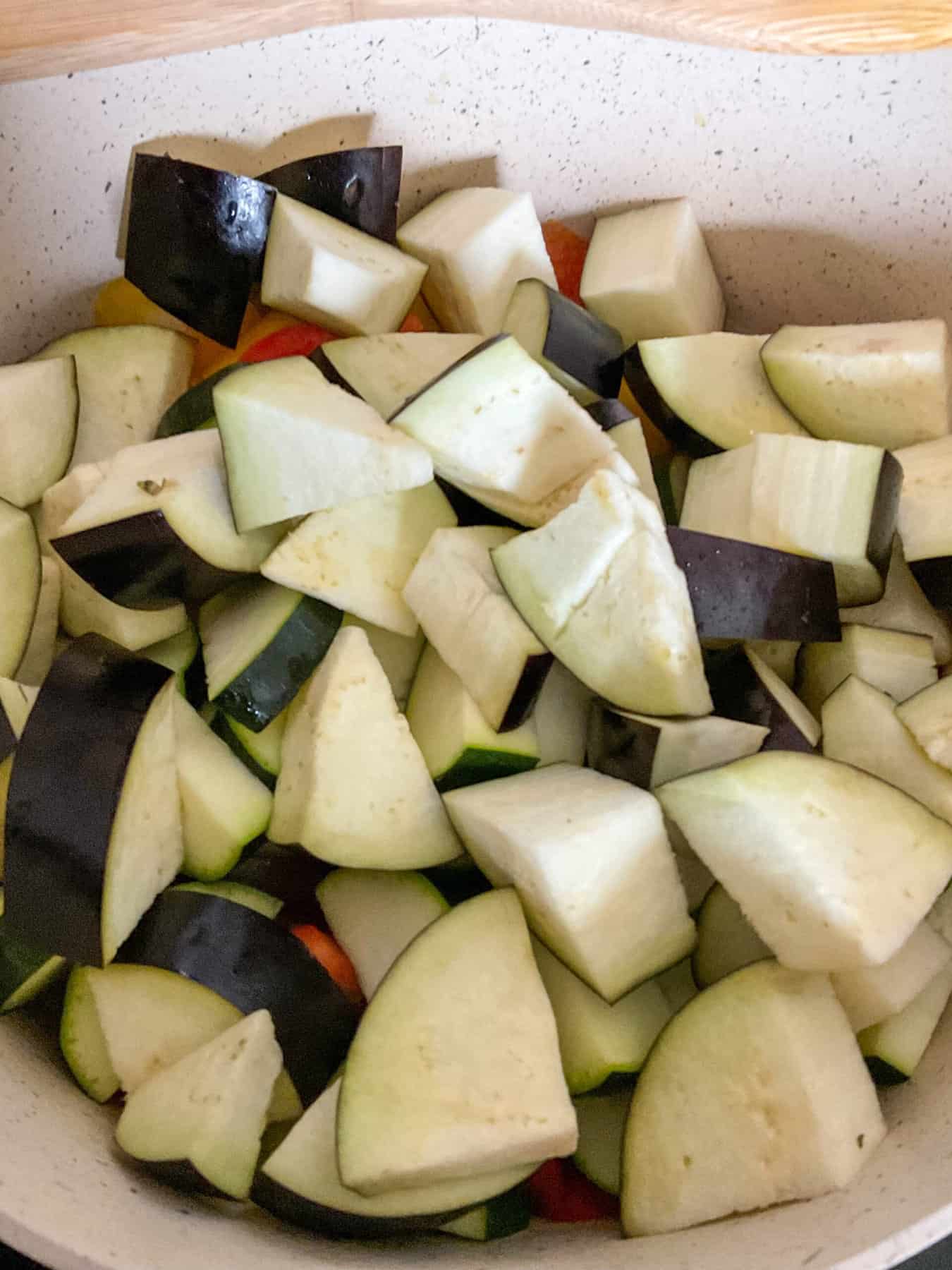 Aubergine added to ratatouille stew in pot.