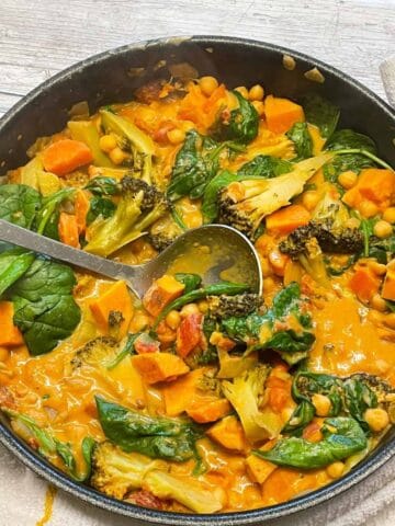 Red Thai curry cooked and in pan ready to be served with a silver ladle.
