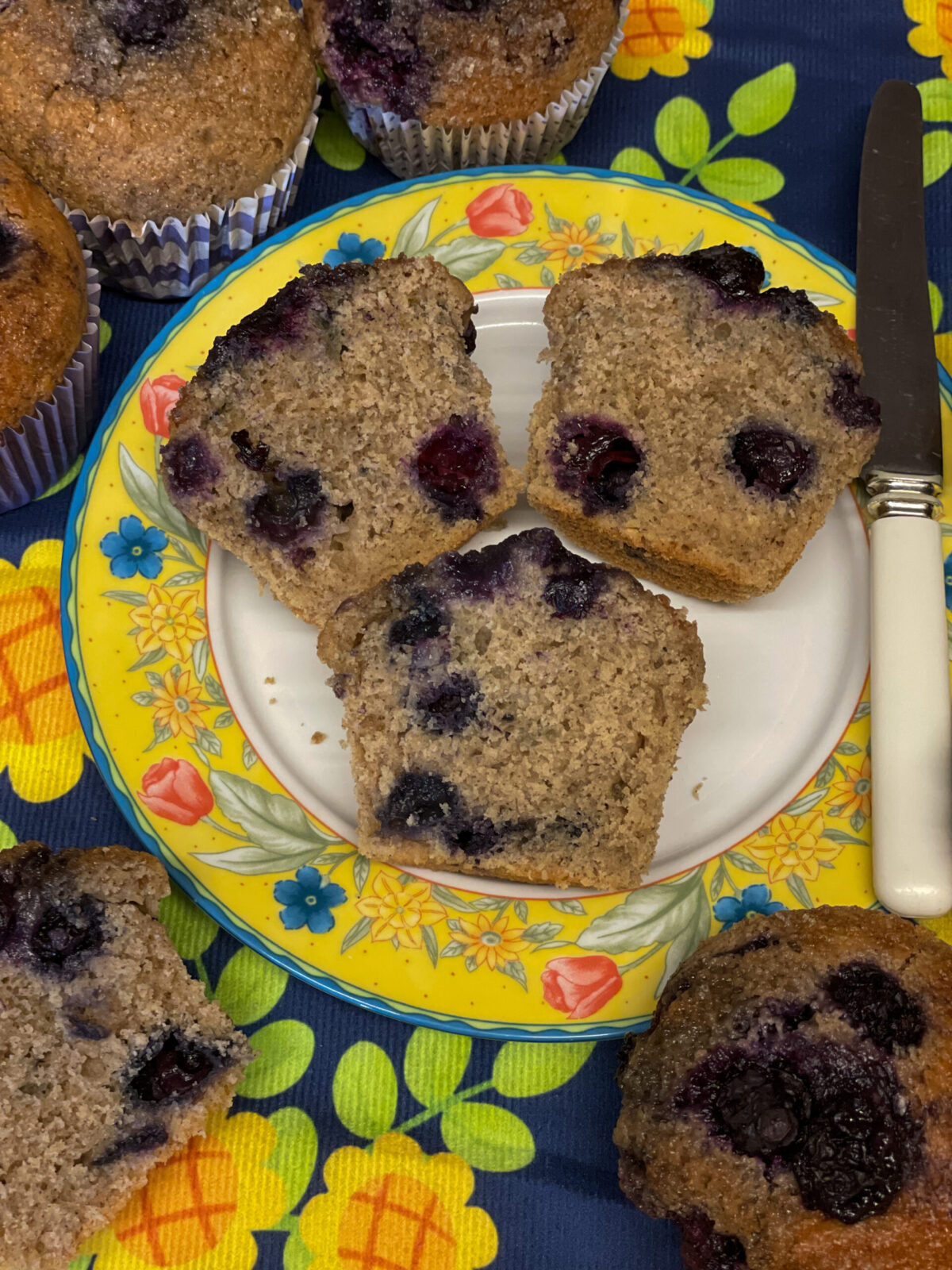 Blueberry muffins variation sliced so that the insides can be viewed. on a flower patterned plate and more muffins around the side.