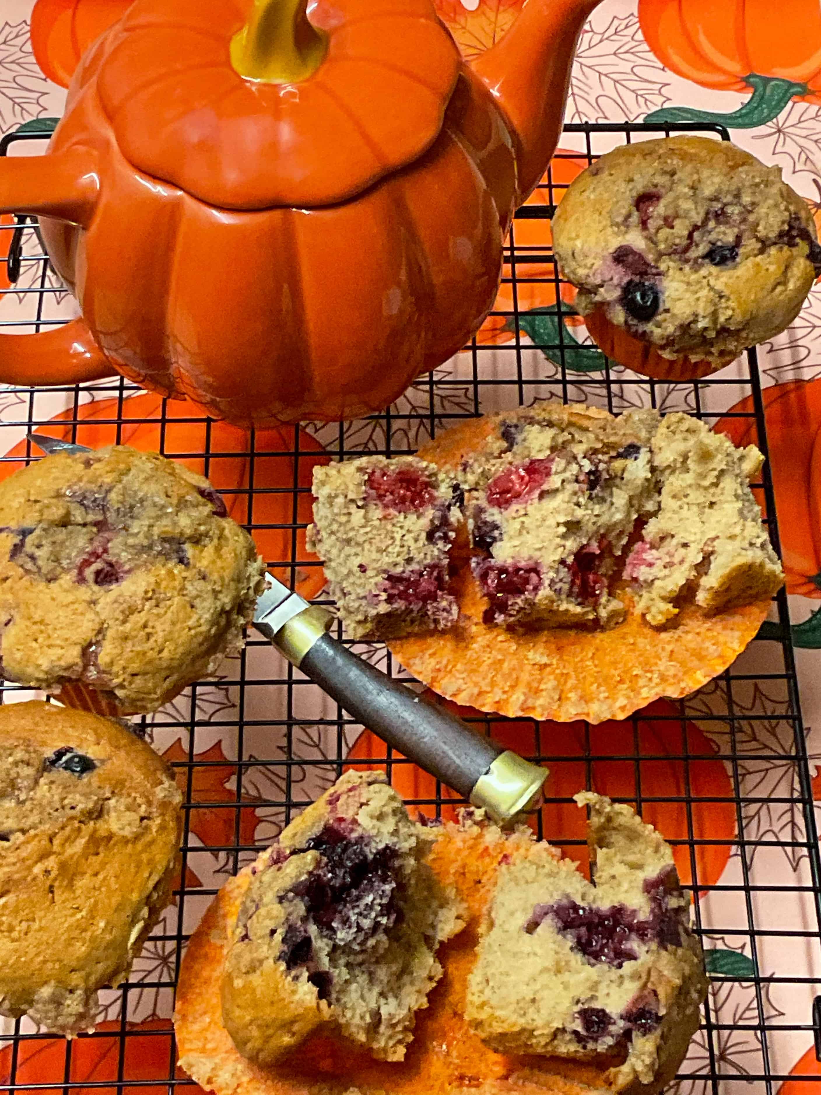 Mixed berry muffin variation sliced to see the insides, pumpkin teapot in background and pumpkin image table cloth in background.
