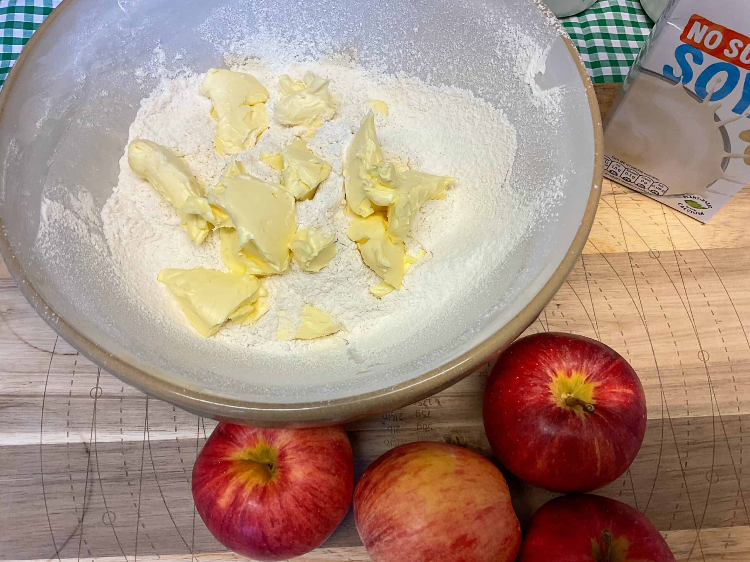 Flour and margarine added to mixing bowl with red apples to side on the cutting board.