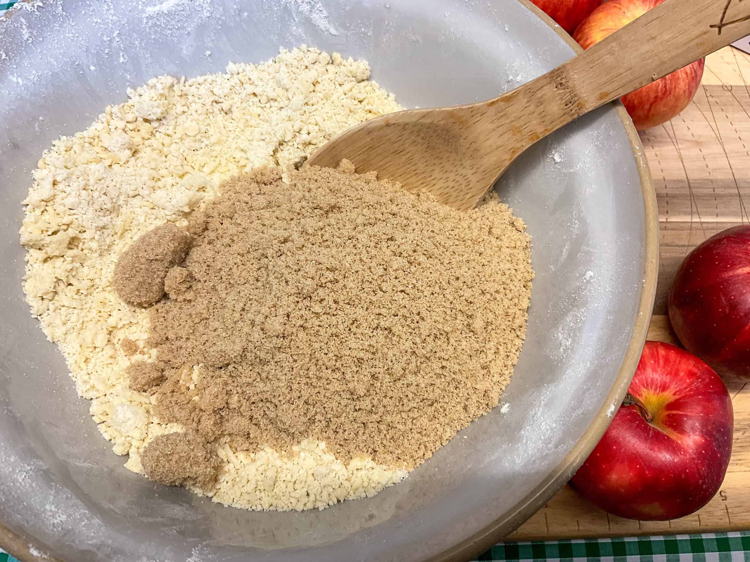 Brown sugar added to mixing bowl with wooden spoon to side.