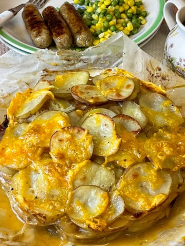 A Welsh onion cake on a serving plate with a dinner plate in background with vegan sausages and peas and corn.