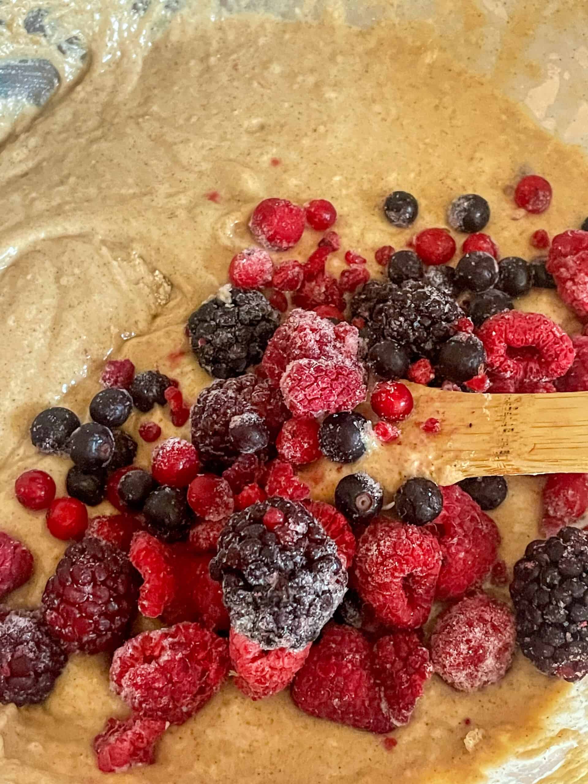 Mixed berries added to muffin mixture in mixing bowl.