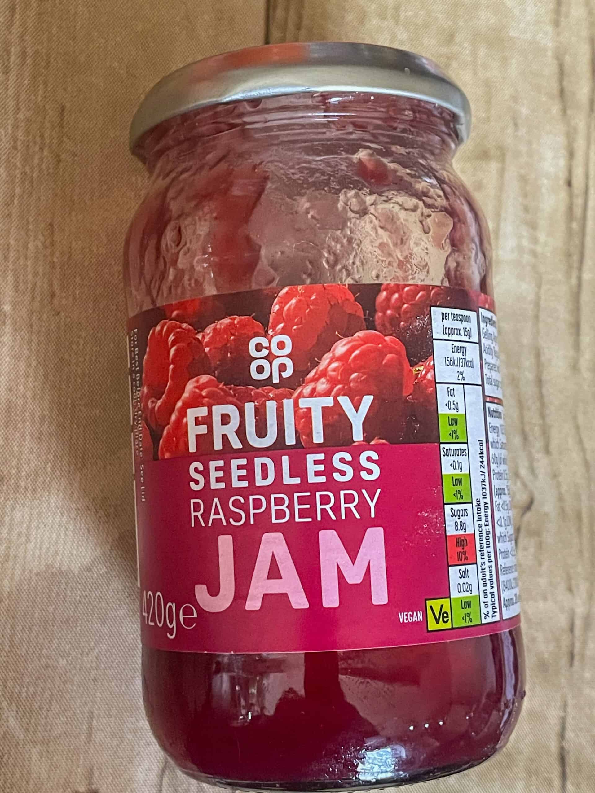 A jar of raspberry jam on a cutting board.