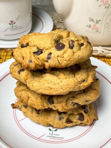 A pile of vegan chocolate chip cookies on a vintage flower patterned plate with matching teapot in back ground.