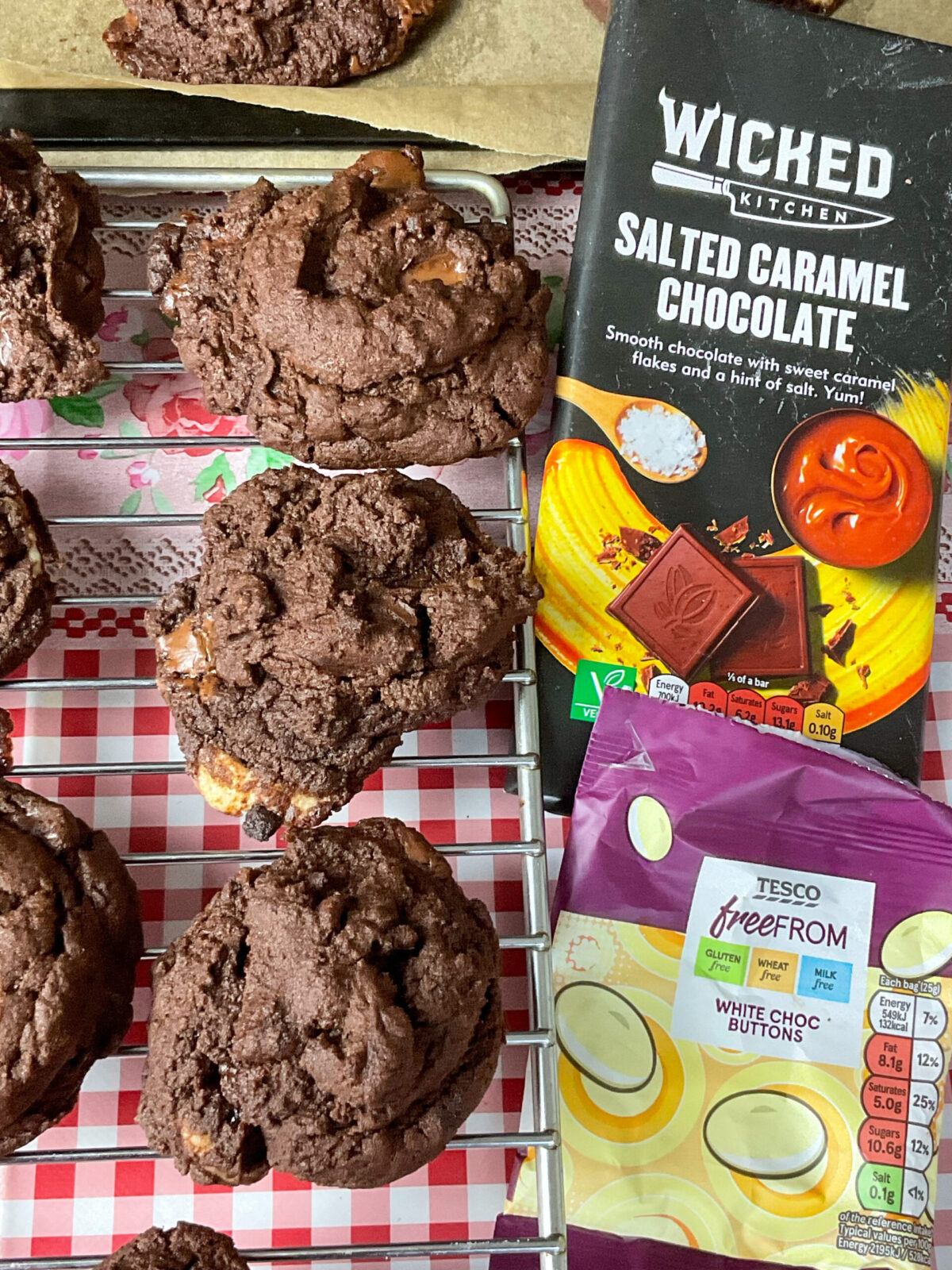 A batch of cookies prepared with a bar of salted caramel chocolate and dairy-free white chocolate buttons to the side of the cooling rack.