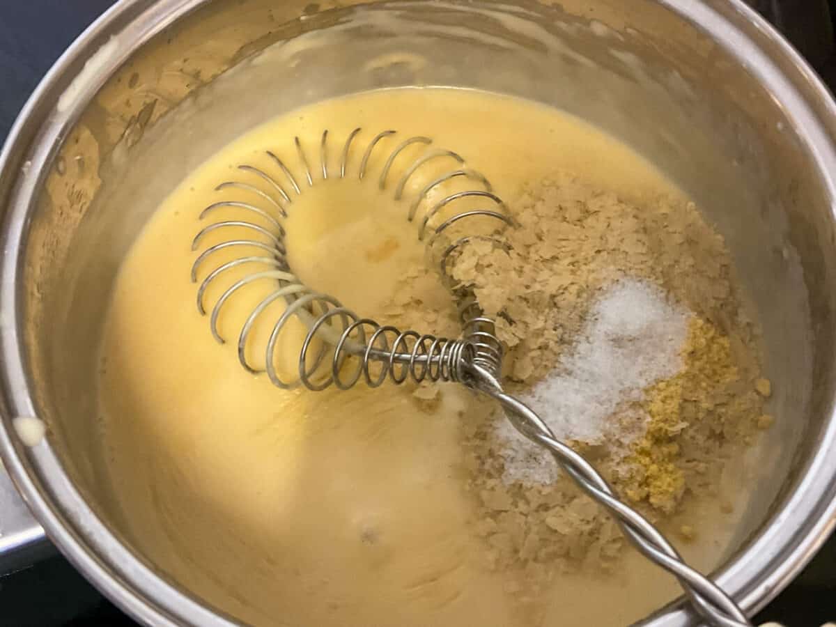 Seasonings added to vegan cheese sauce in saucepan with a metal hand whisk.