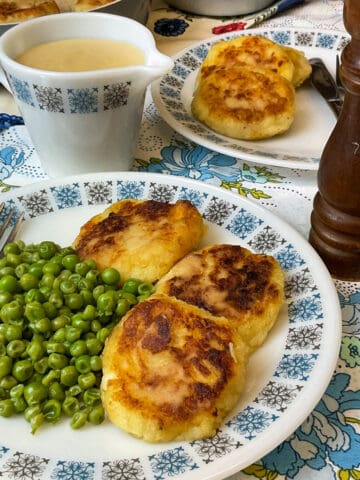 Parsnip patties served on blue flower patterned vintage plate with matching jug to side filled with cheese sauce.