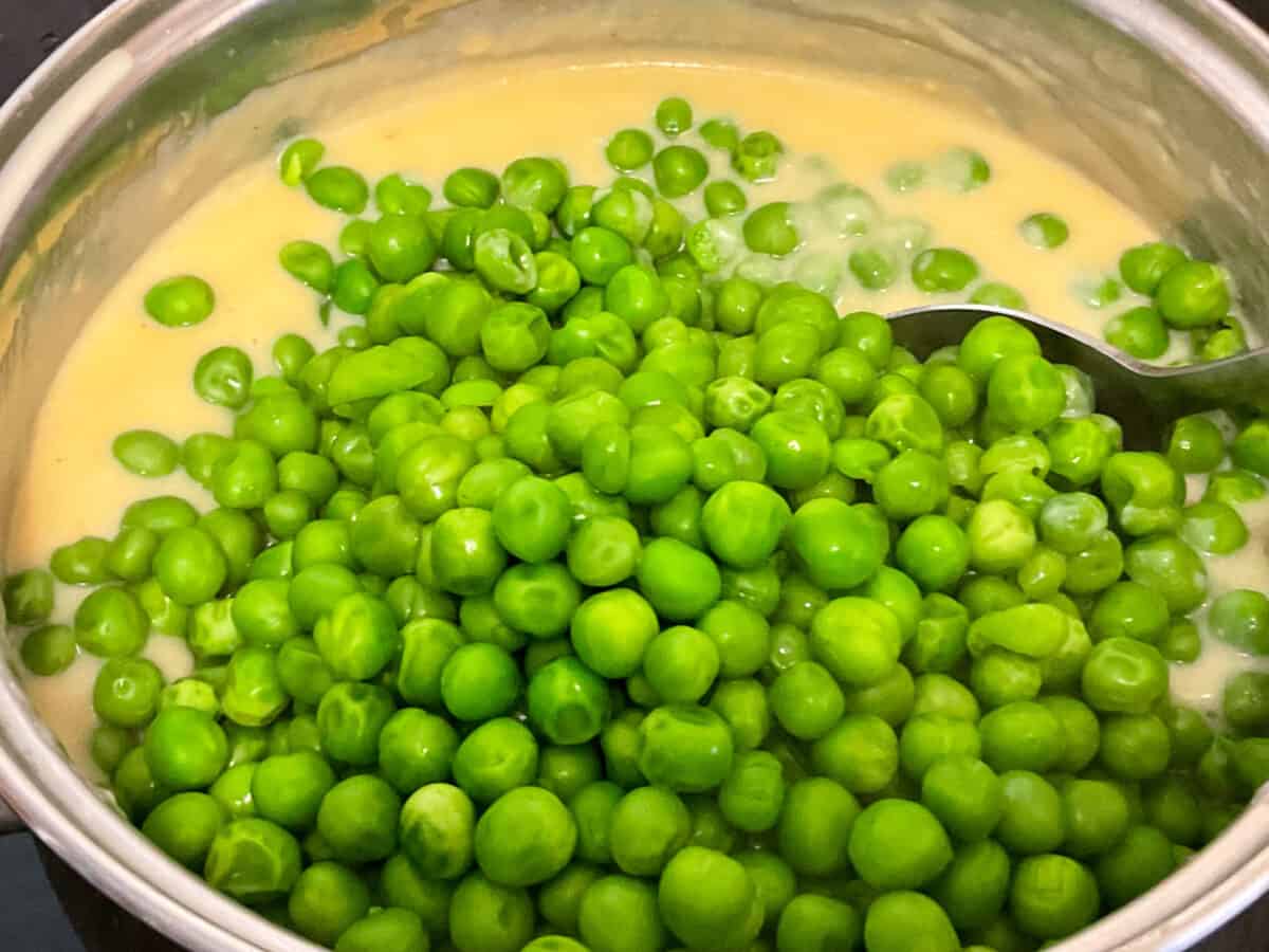 Peas added to cheese sauce in saucepan.