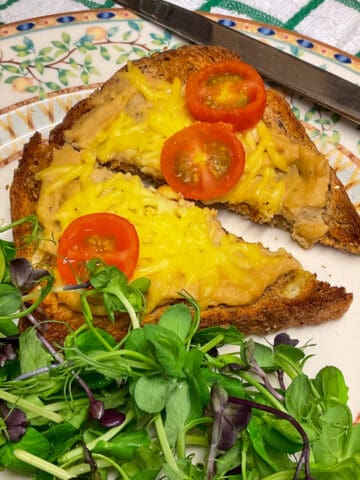 Vegan Welsh rarebit served with salad on a plate with cutlery to side, featured image.
