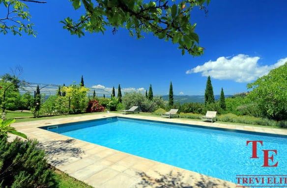 Luxurious swimming pool overlooking scenic Italian countryside with cypress trees and lush greenery, showcasing premium outdoor living space.