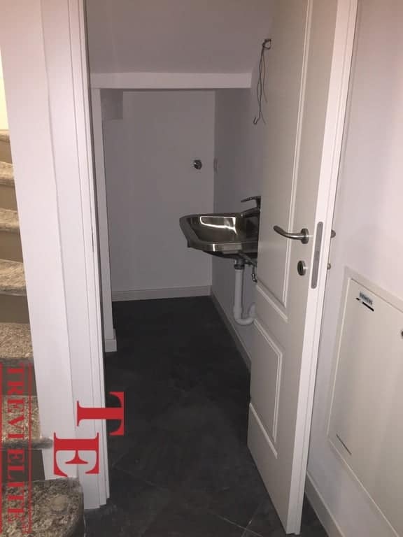 Small utility sink in a compact space with plain white walls and a door partially open, showcasing a functional yet minimalistic design ideal for a modern Italian home.