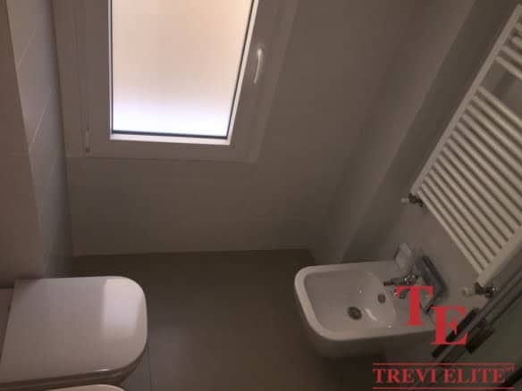 Modern small bathroom with a white bidet, a towel radiator, and a frosted window for natural light. The space is clean, bright, and efficiently designed for comfort and functionality.